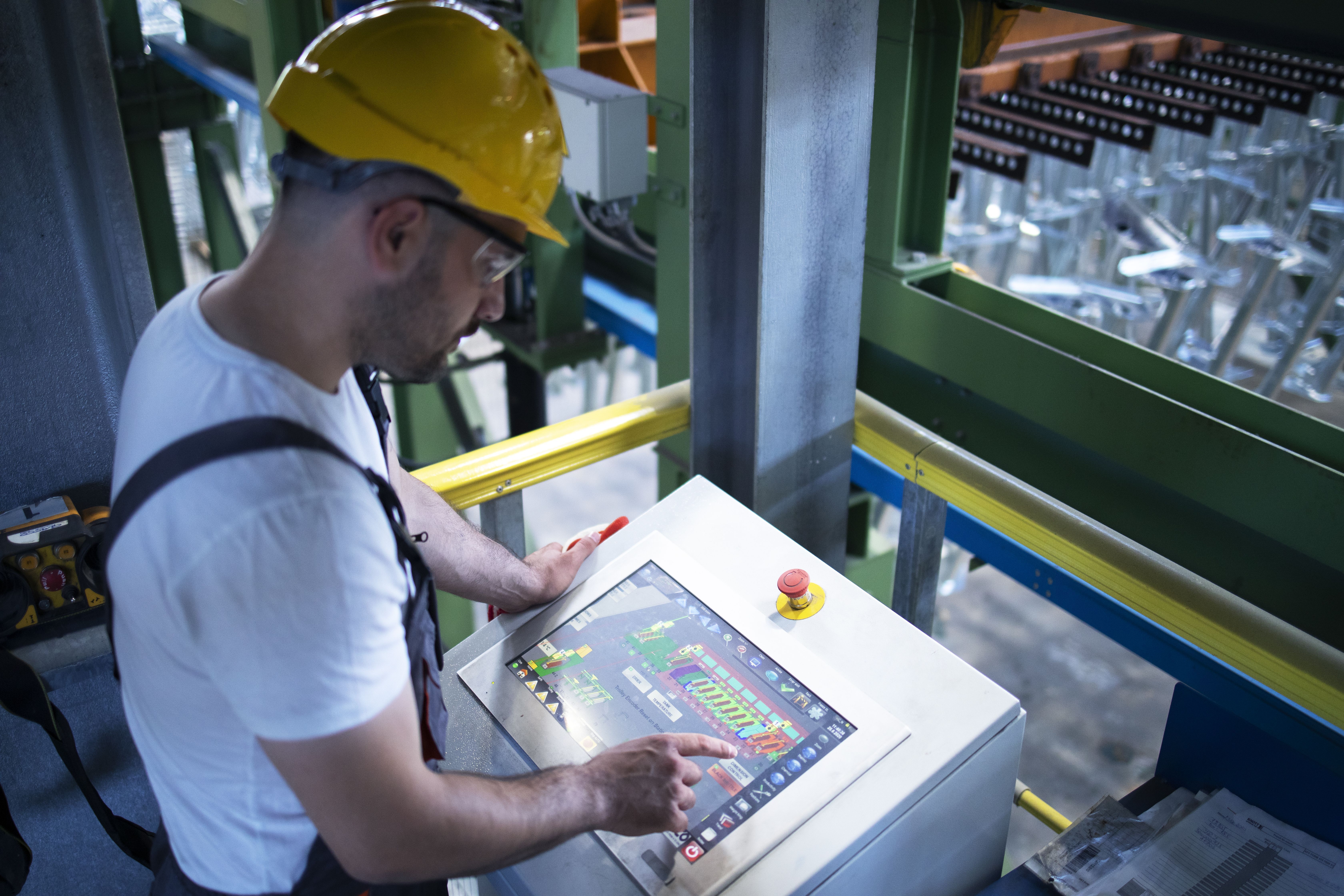Operário de fábrica monitorando máquinas industriais e a produção remotamente em uma sala de controle.