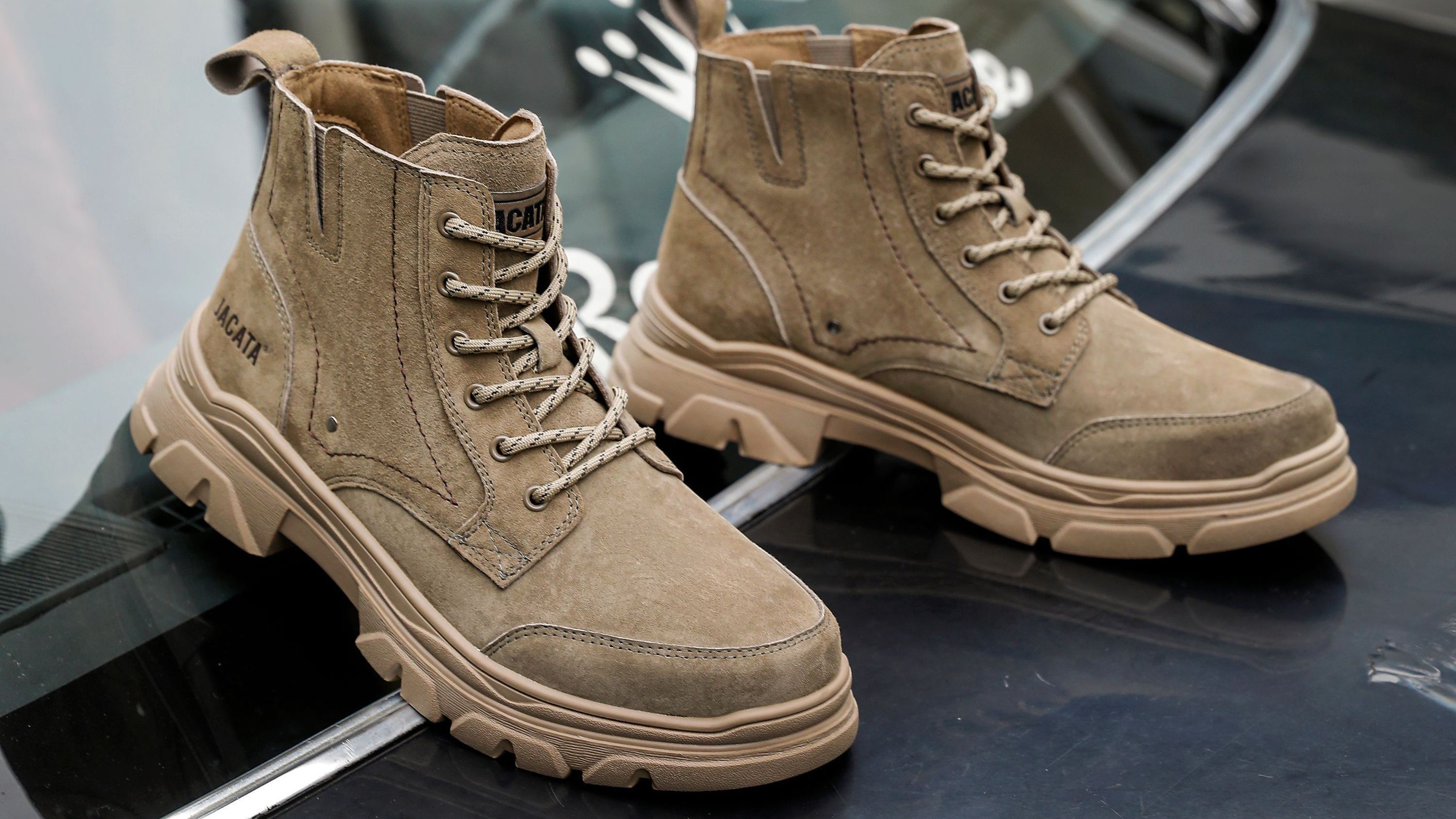 Sapatos de camurça marrons posicionados em cima do vidro dianteiro de um carro preto