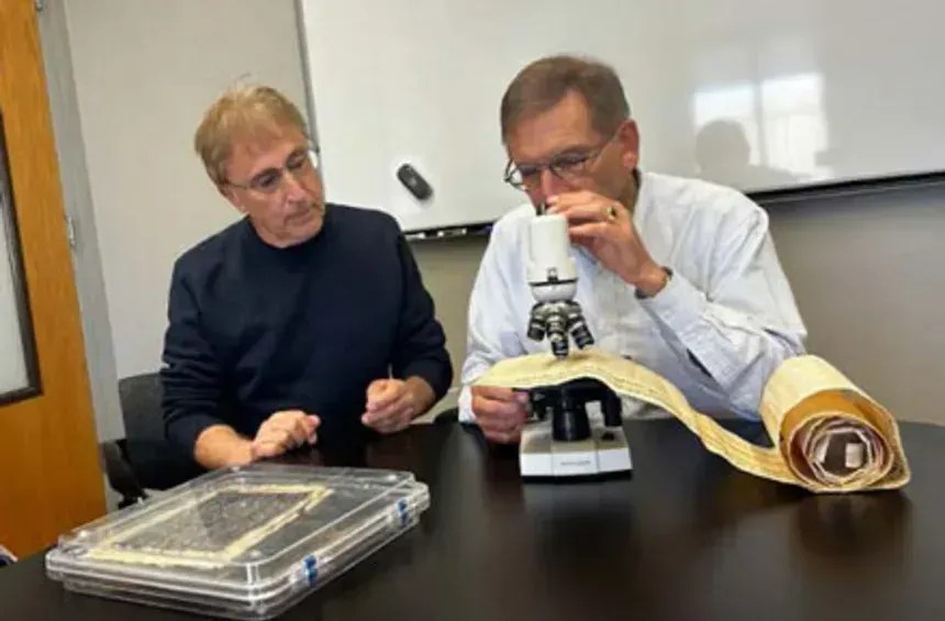 O físico Karl van Bibber (à direita), professor da UC Berkeley, examina a tinta em uma réplica de pergaminho para confirmar os cálculos de densidade do chumbo, enquanto Douglas Seiler, pesquisador voluntário da UC Berkeley, observa. • Cortesia de Douglas Seiler