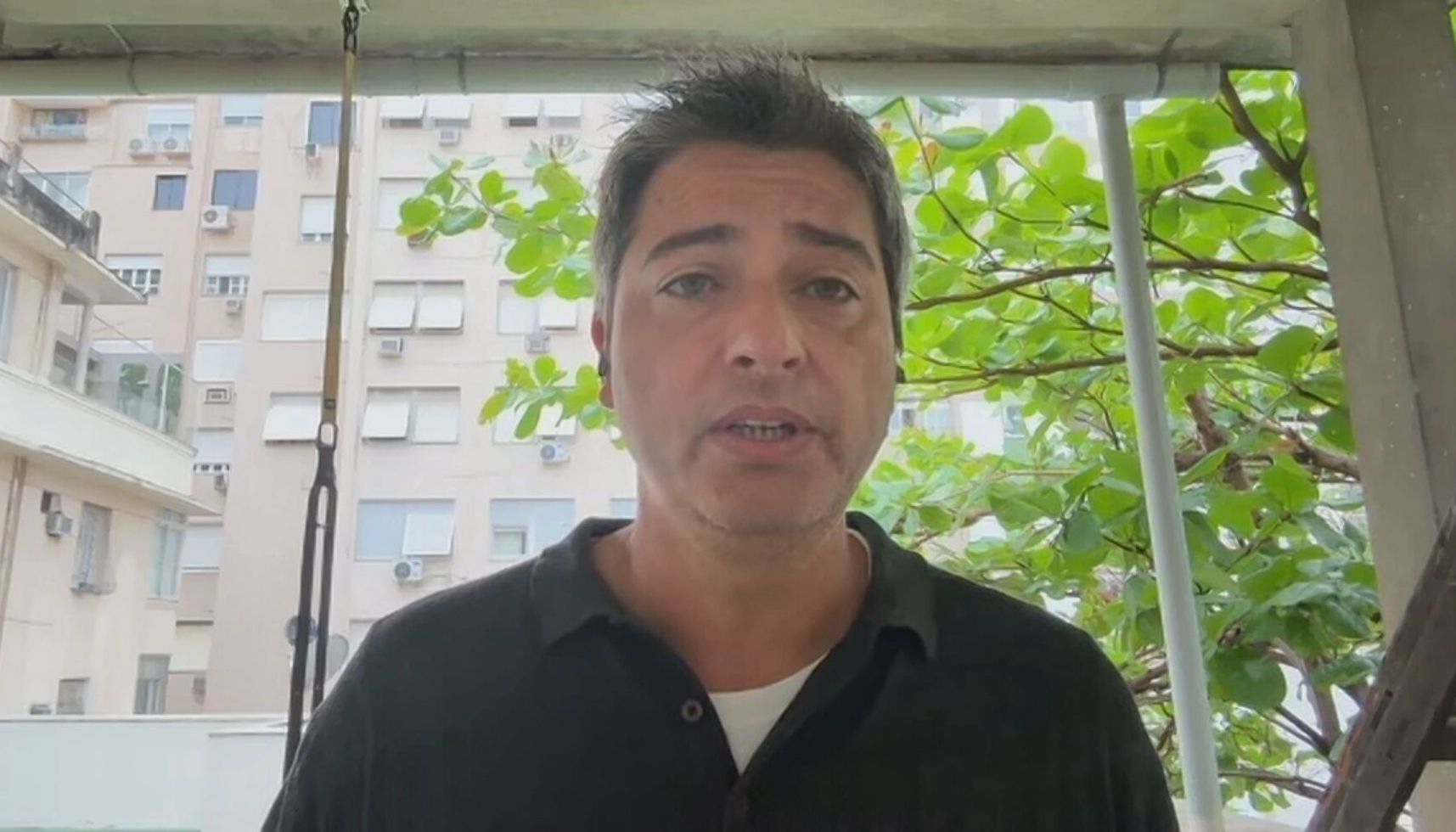 Senador Carlos Portinho com uma camisa preta em frente a uma janela que mostra prédios e árvores ao fundo