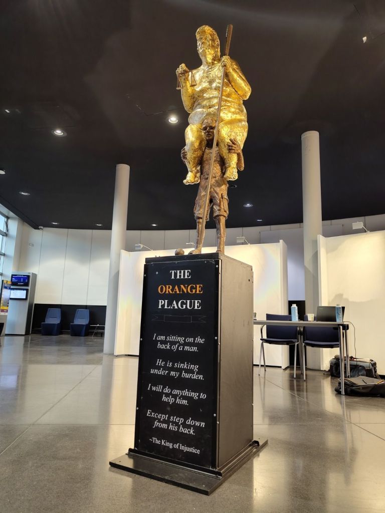 Uma escultura satírica representando Donald Trump nu e coberto de ouro, sentado nas costas de um homem frágil, será exibida no Parlamento Europeu, em Estrasburgo.