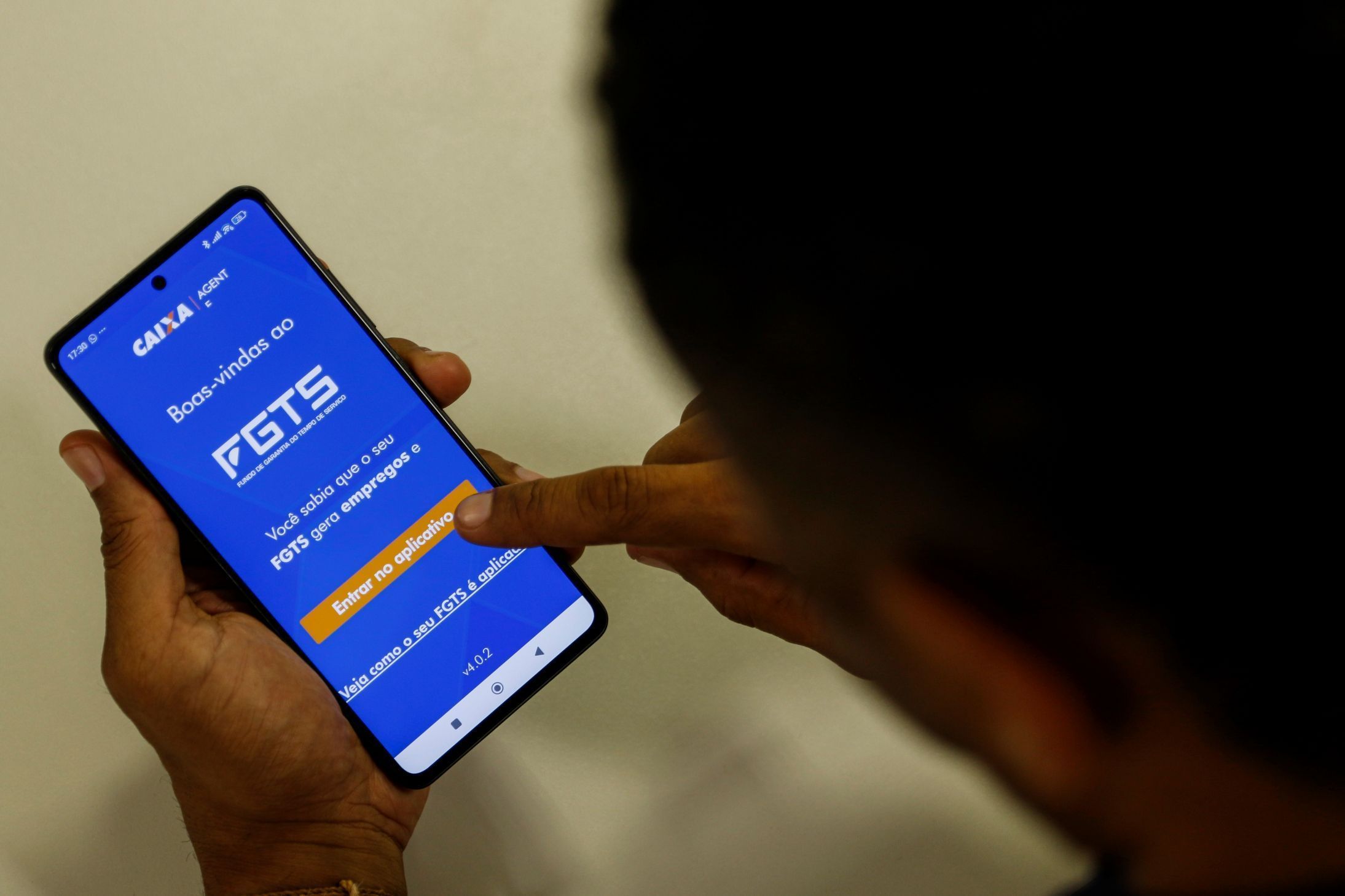 Um homem segura um celular com a imagem da página inicial do aplicativo FGTS, a tela é azul escrito FGTS em branco