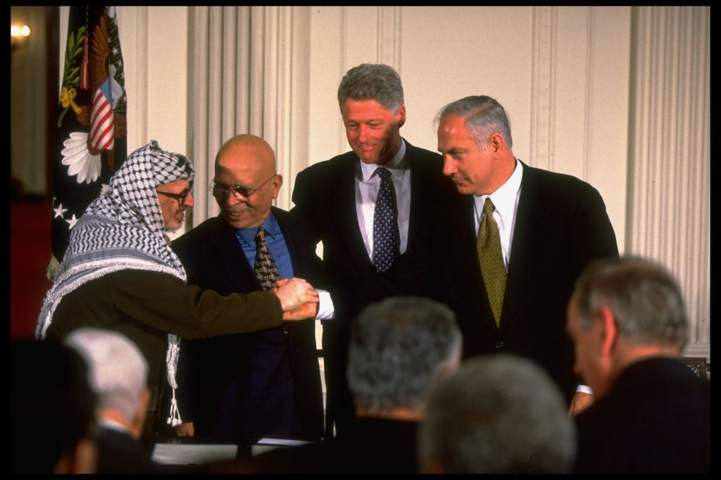 O líder palestino Yasser Arafat, o rei Hussein da Jordânia, o presidente Bill Clinton e o primeiro-ministro israelense Benjamin Netanyahu, durante os cumprimentos na cerimônia de assinatura do acordo de paz de Wye, na Casa Branca