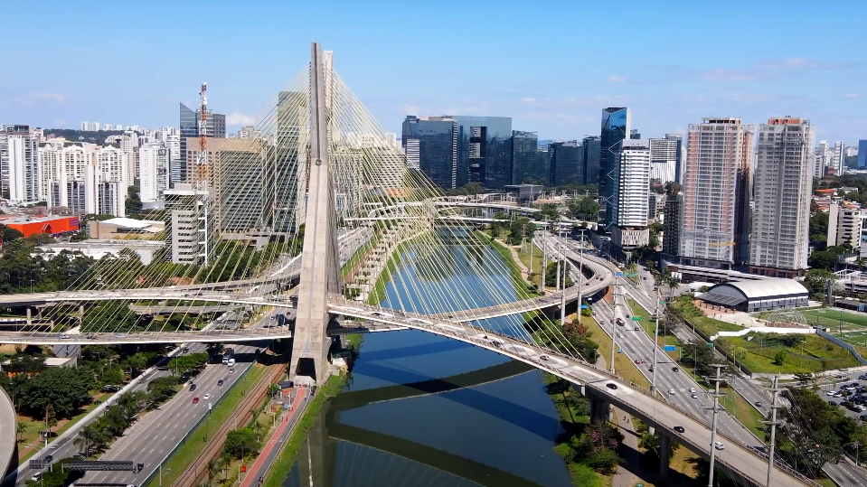 Vista aérea da ponte estaiada Octávio Frias de Oliveira sobre um rio em São Paulo, cercada por prédios altos e estradas.