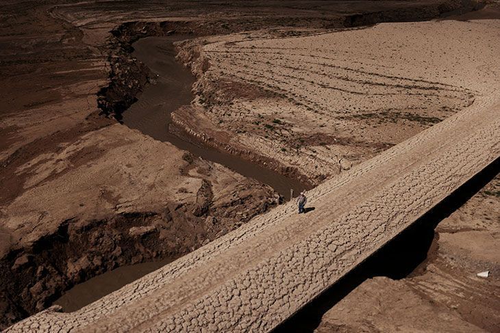 Um homem caminhava sobre o solo rachado de um reservatório que estava secando durante a seca extrema na Catalunha, Espanha, em 2023. • REUTERS/Nacho Doce