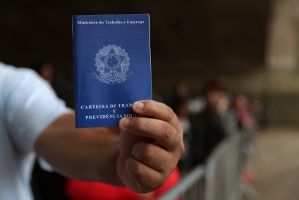 Pessoa mostra carteira de trabalho em fila de emprego em