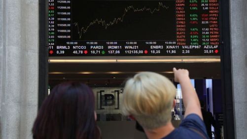 Pessoas apontam para painel mostrando cotações na B3
