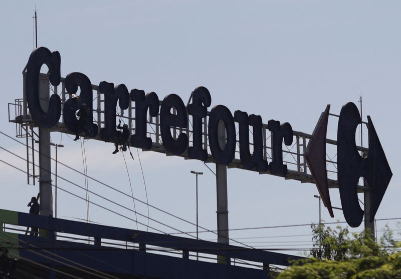 Trabalhadores fazem manutenção no logotipo de um supermercado Carrefour no