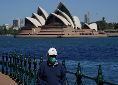 Homem com máscara caminha em frente à Casa da Ópera de Sydney; Austrália registra crescimento dos casos de Covid-19