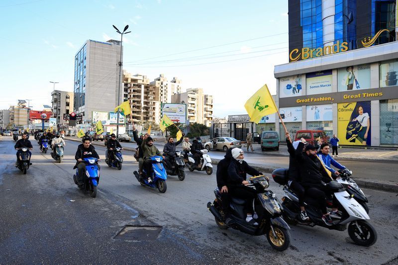 Homens carregam bandeiras do Hezbollah enquanto andam de moto, na